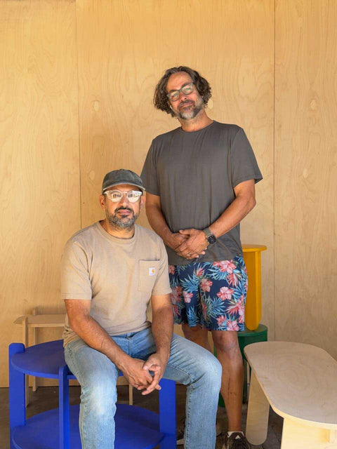 Two men standing in a minimalist wooden space, showcasing creativity and friendship in design.