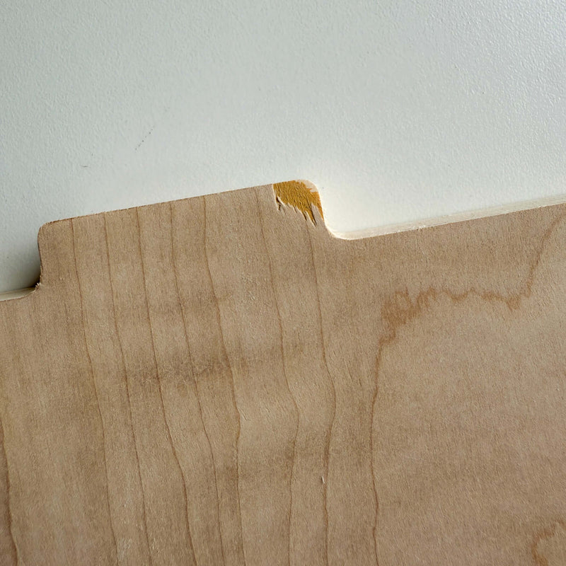 Close-up of wood panel with a small blemish showing chip and grain details, highlighting unique furniture imperfections.
