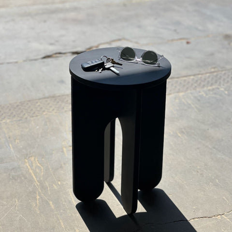 Stylish black stool with sunglasses and keys on a concrete floor, perfect for modern living spaces.