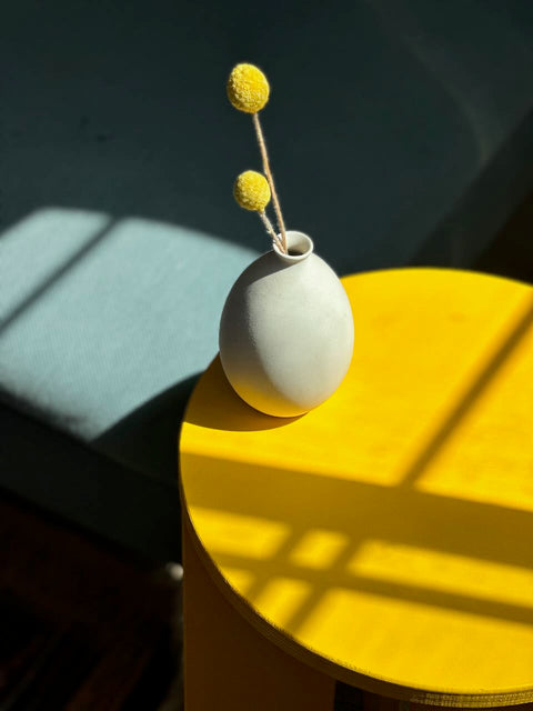 Minimalist vase with yellow flowers on a bright yellow table, highlighted by natural light shadows.