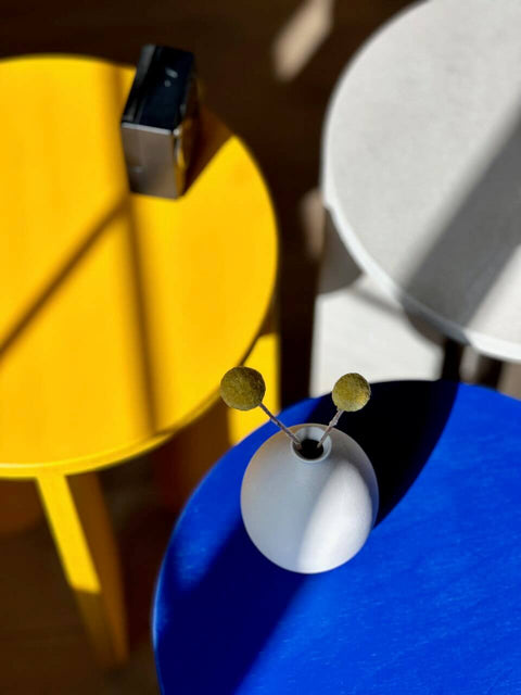 Colorful round tables in yellow, blue, and grey with a white vase and decorative elements.