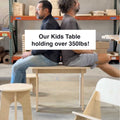 Two men sitting back to back on a strong eco-friendly kids table, showcasing its durability holding over 350lbs.
