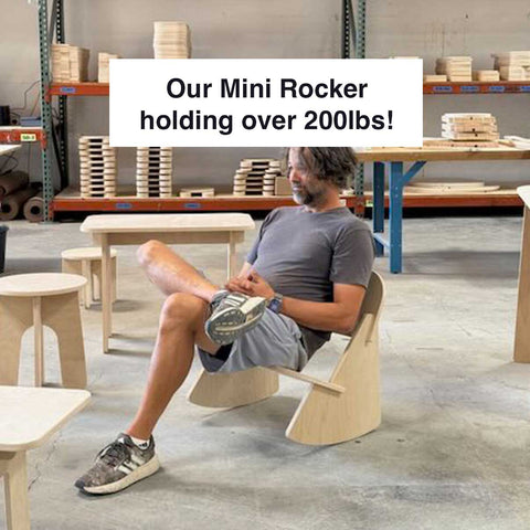 Man sitting on a Mini Rocker, demonstrating its strength, supporting over 200lbs in a workshop setting.