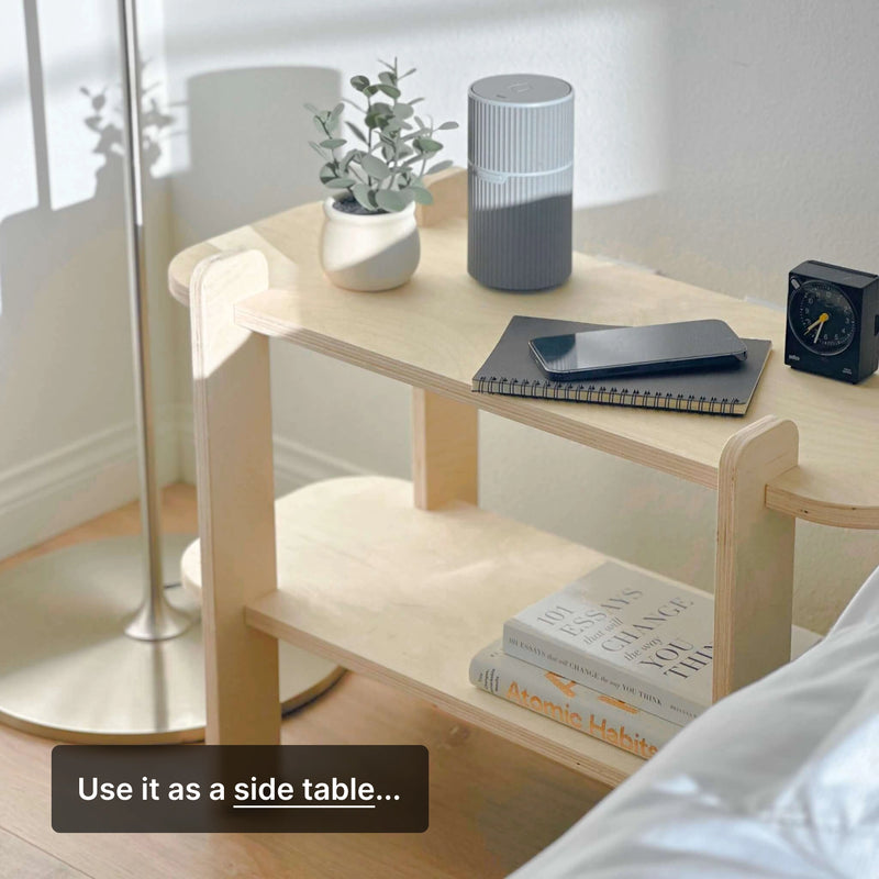 Minimalist side table with books, notebook, plant, clock, and speaker in a stylish bedroom setting.