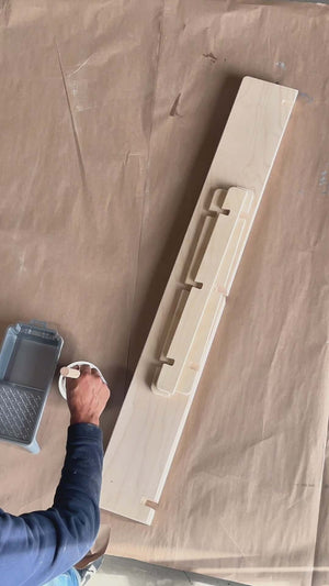 A person painting an unfinished wall shelf on a brown surface, showcasing DIY customization options.