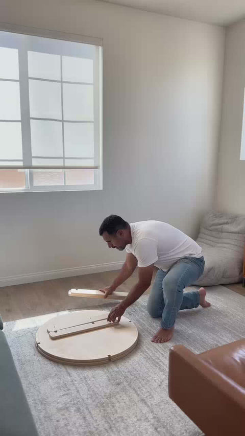 Man assembling a round coffee table on a rug in a bright living room, showcasing easy setup and stylish design.