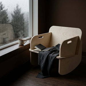 Modern Rocker with a cozy throw and books by a rain-soaked window, showcasing its sleek design.