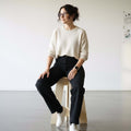 Woman sitting on A-Stool made of birch plywood, showcasing its clean lines and solid build in a modern space.